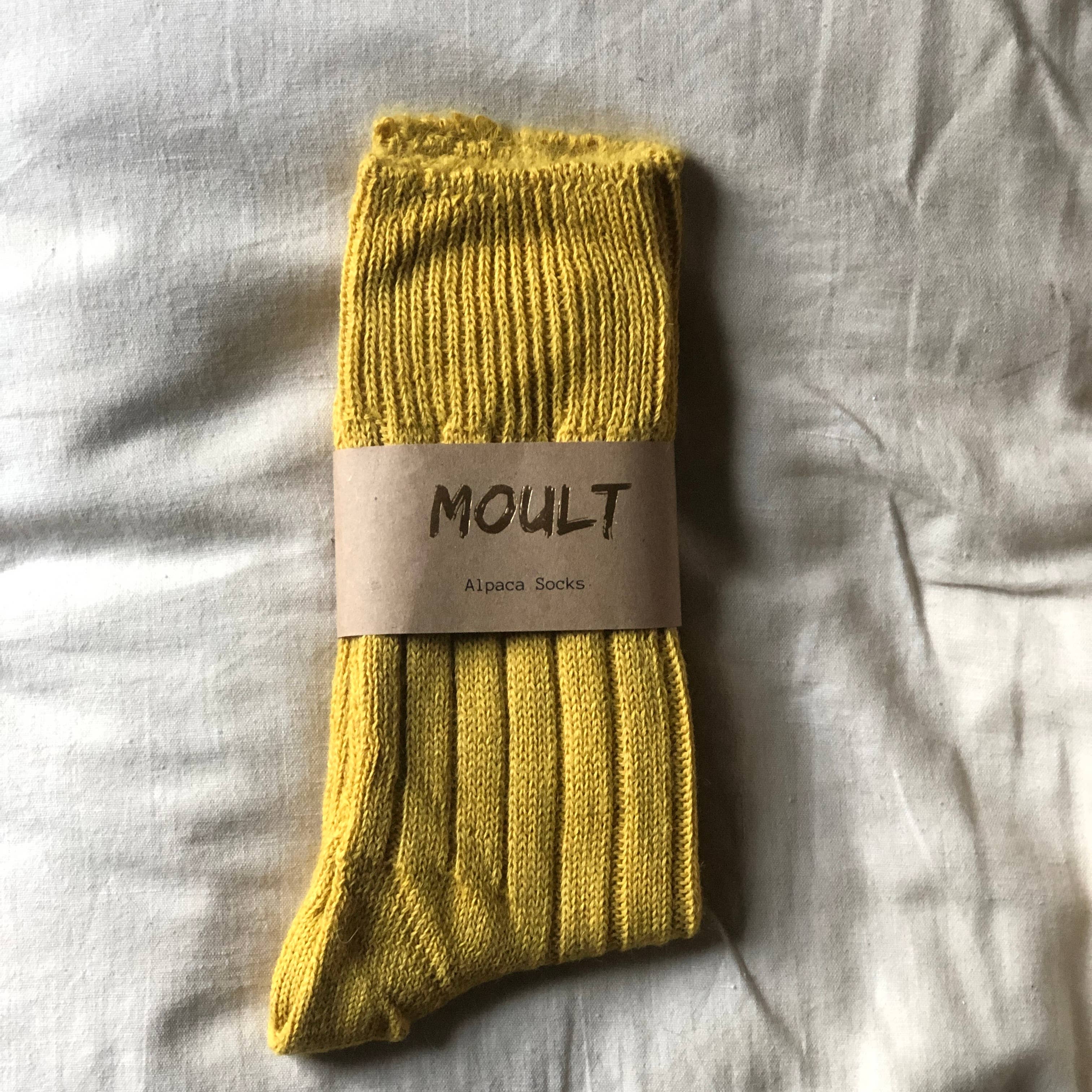 Yellow sock with 'Moult' label on a light gray fabric background