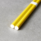 Two yellow chopsticks with white ends on a gray surface