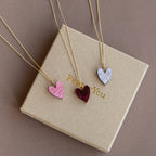 Three heart-shaped pendants on gold necklaces on a beige box.