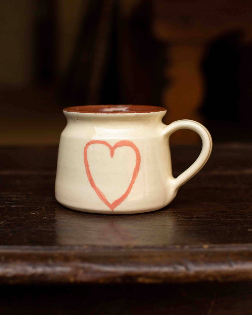 White mug with a red heart design on a dark wooden surface