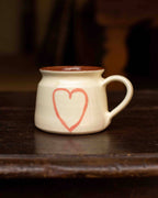 White mug with a red heart design on a dark wooden surface