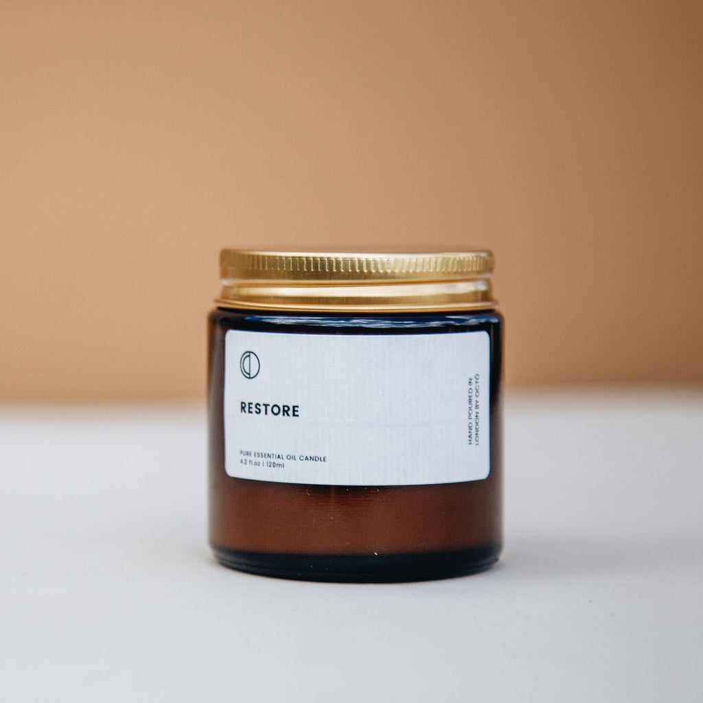 Candle jar labeled 'RESTORE' with a gold lid on a beige background