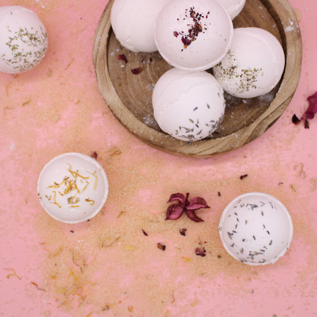 Bath bombs with floral toppings in a wooden bowl on a pink surface