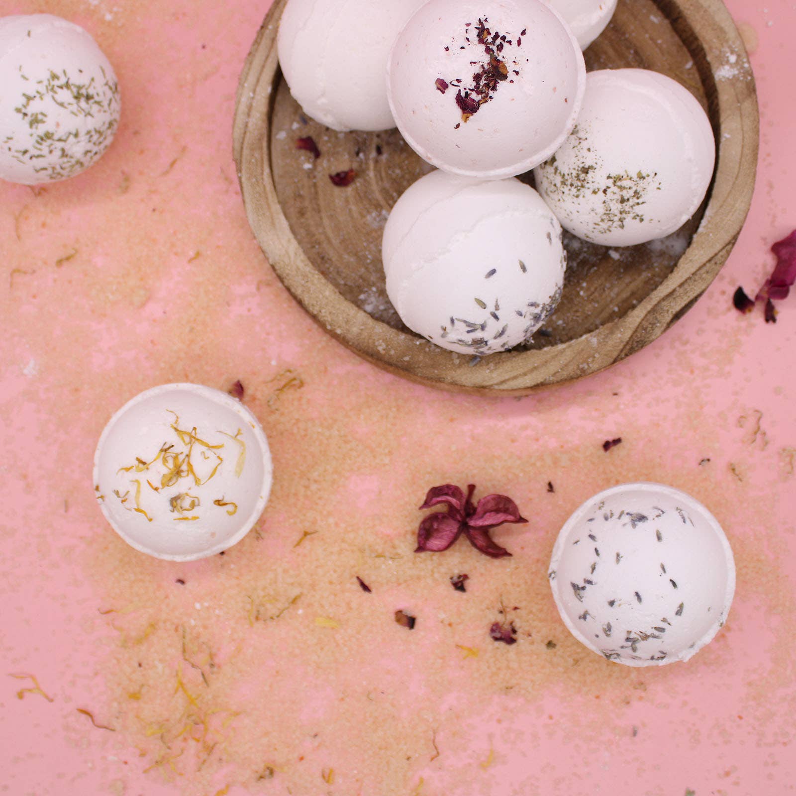 Bath bombs with floral toppings in a wooden bowl on a pink surface