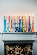 Colorful candles on a mantelpiece with logs below