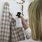 Person using a garment refresher on a checkered shirt with a blurred background