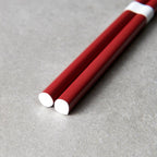 Two red chopsticks with white ends on a gray surface