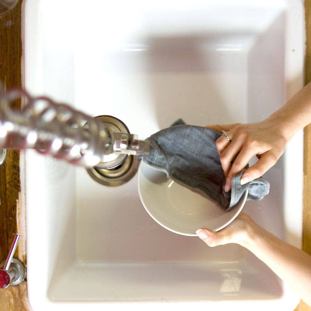 Person cleaning a plate with a cloth under running water from a tap.