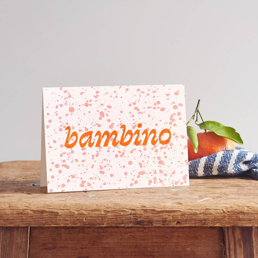 pink and orange Bambino Baby Greeting Card for New Baby on a wooden table. 