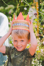 Child wearing a birthday hat outdoors with greenery in the background