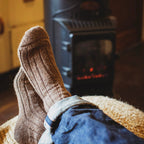 Person wearing soft brown socks and blue jeans with a fireplace in the background