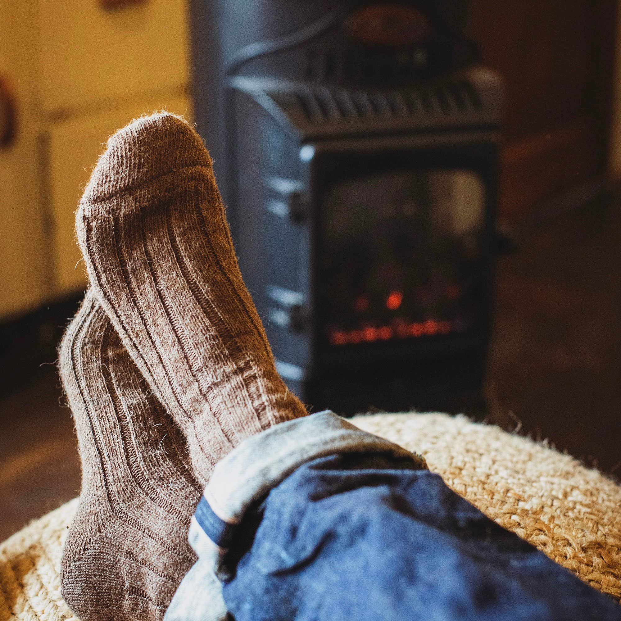 Person wearing soft brown socks and blue jeans with a fireplace in the background