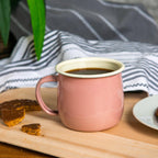 Pink mug with white interior on a wooden surface with cookies and a striped cloth in the background