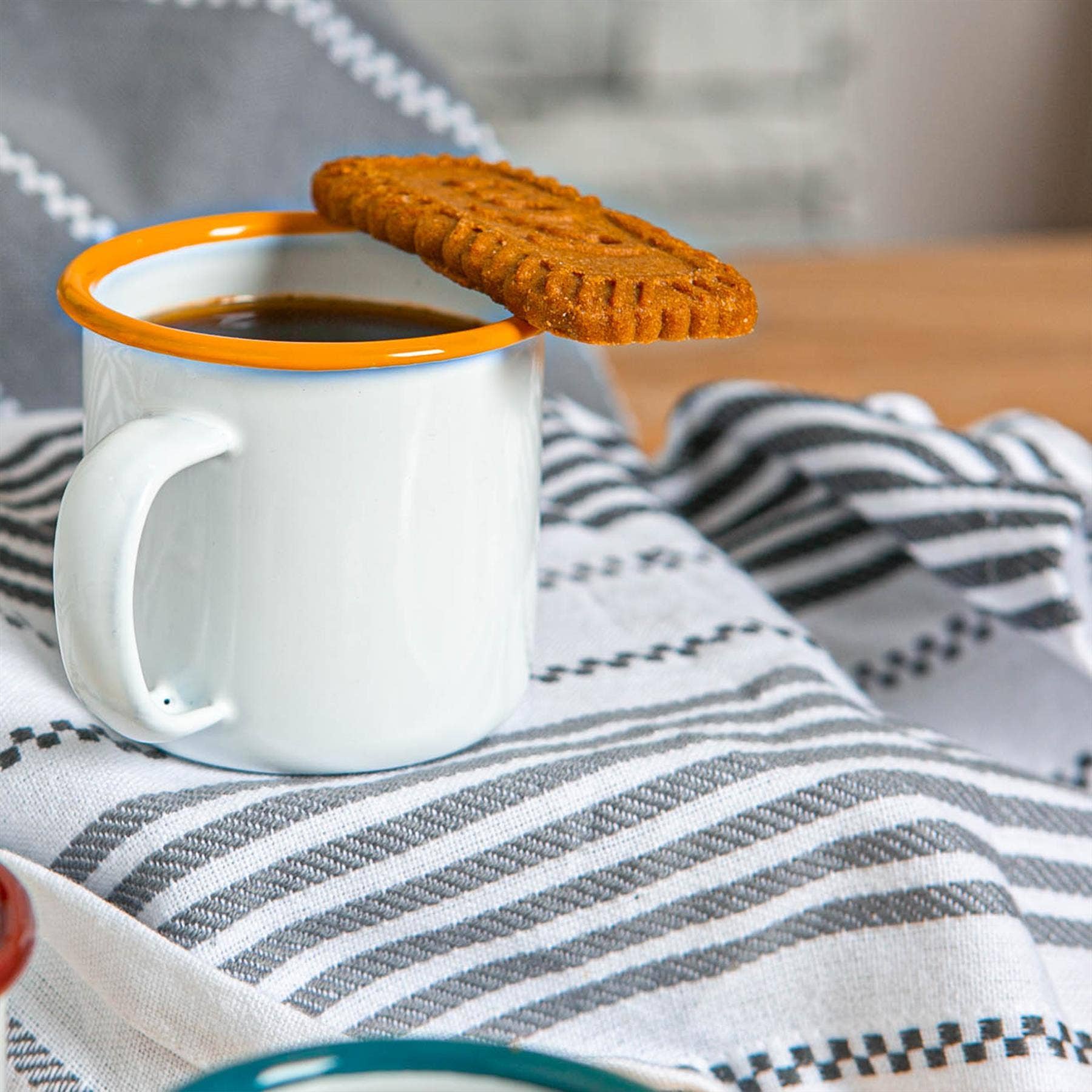 White mug with orange rim containing coffee, placed on a striped fabric surface.