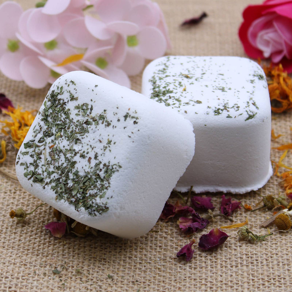Two white bath additives with green herbs on a textured surface with flowers and petals.