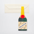 Tall rectangular greetings card featuring champagne bottle design and cream envelope on a grey background - All Good Things