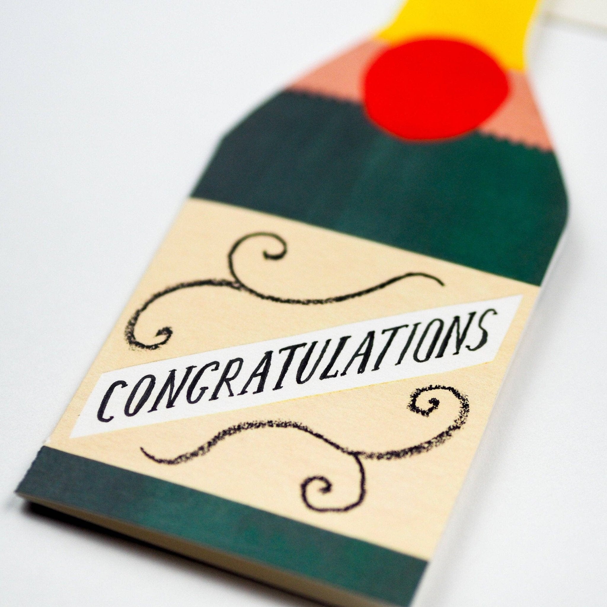 Close up of tall rectangular greetings card featuring champagne bottle design on a grey background - All Good Things