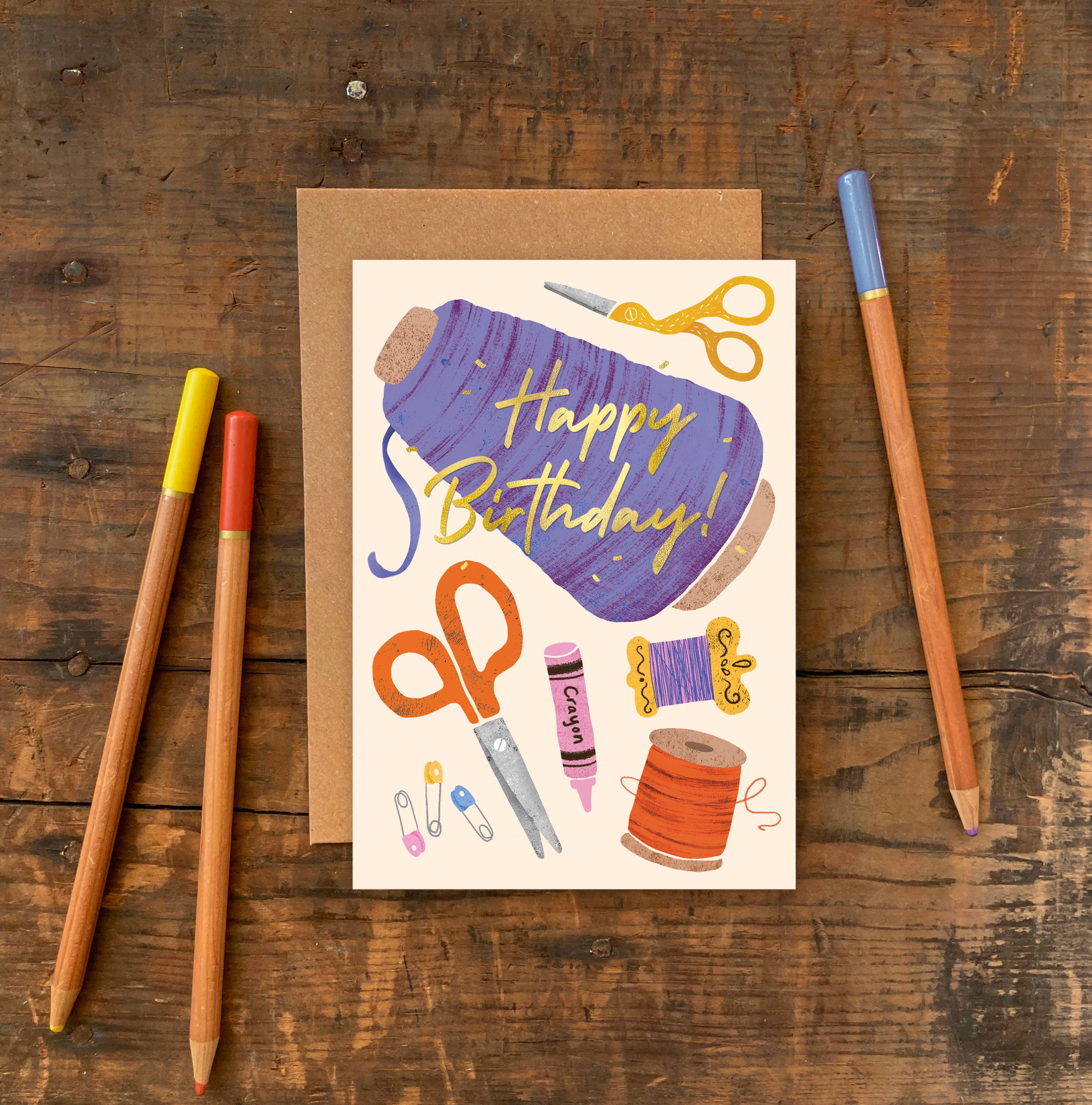 crafting and sewing birthday card on a wooden table with pencils scattered around