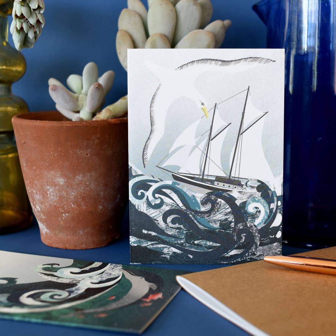 Greeting card with a ship and sea gull  illustration on a blue surface with decorative items