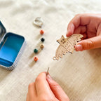 Hand holding a wooden bat with beads and a container on a fabric background