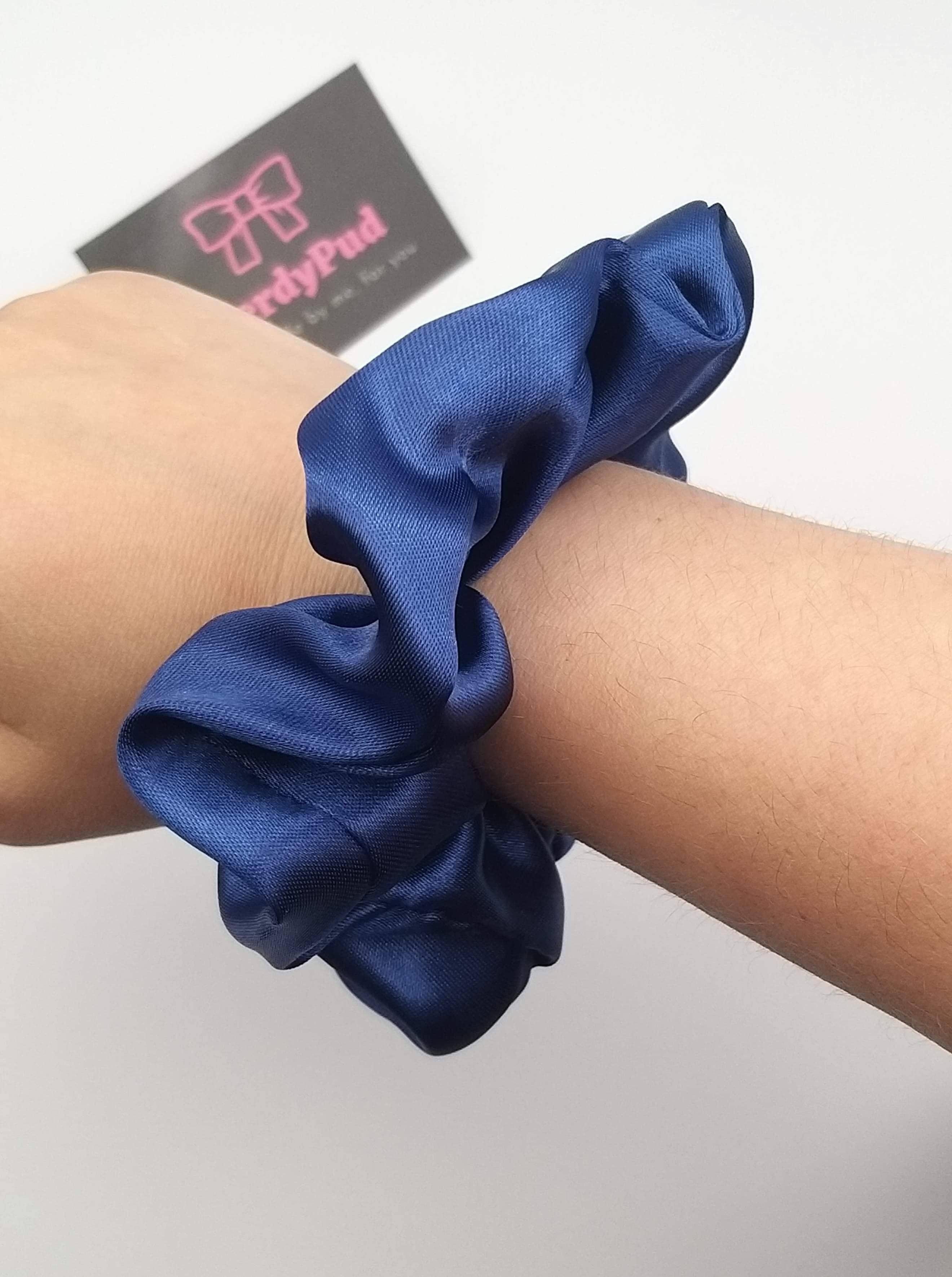 Blue scrunchie on a wrist with a brand card in the background