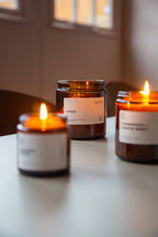 Three lit candles in amber jars with white labels on a blurred background