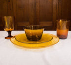 Set of amber glass tableware including a bowl, plates, and glasses on a white surface with wooden background.
