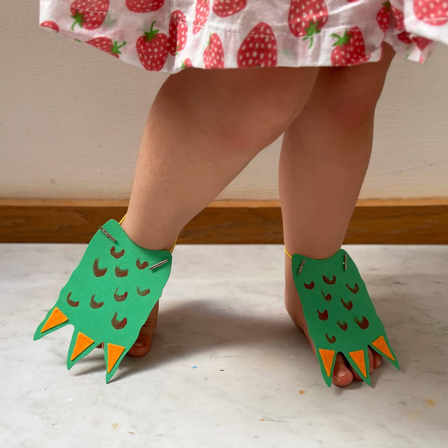 Child wearing green dinosaur-themed shoes on a light wooden floor.