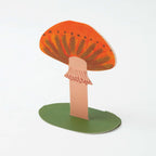 Cardboard cutout of a mushroom with an orange cap and green base on a white background