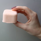 Hand holding a pink bathbomb against a gray background