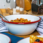 White bowl with red rim containing cereal on a wooden table.