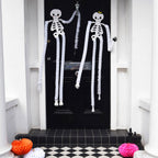 Two Homecomb paper Halloween Skeleton Decorations hung on a black front door - All Good Things