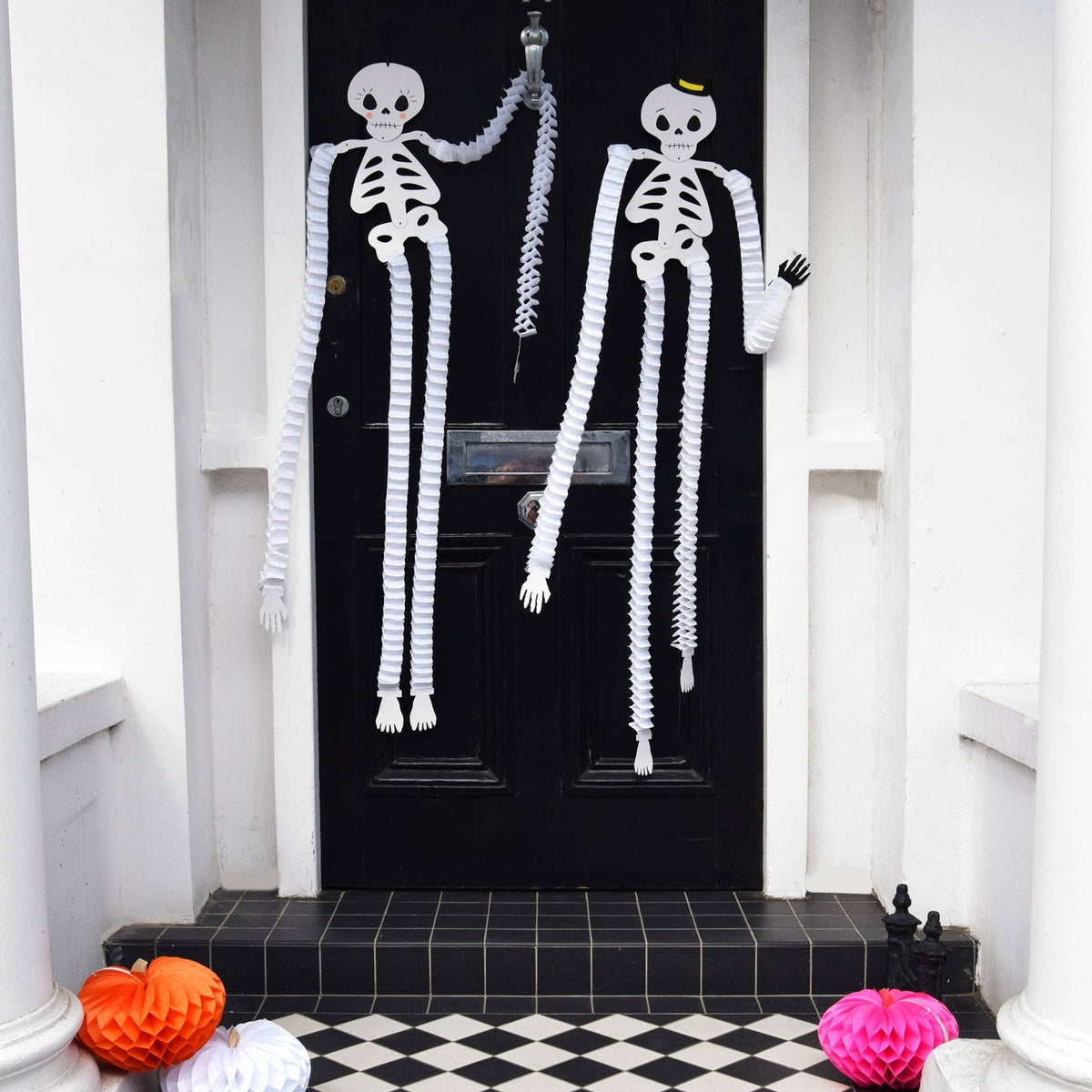 Two Homecomb paper Halloween Skeleton Decorations hung on a black front door - All Good Things
