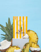 Striped bag of Pina Colada Gummies on a yellow background, styled with fresh coconut and pineapple slices - All Good Things