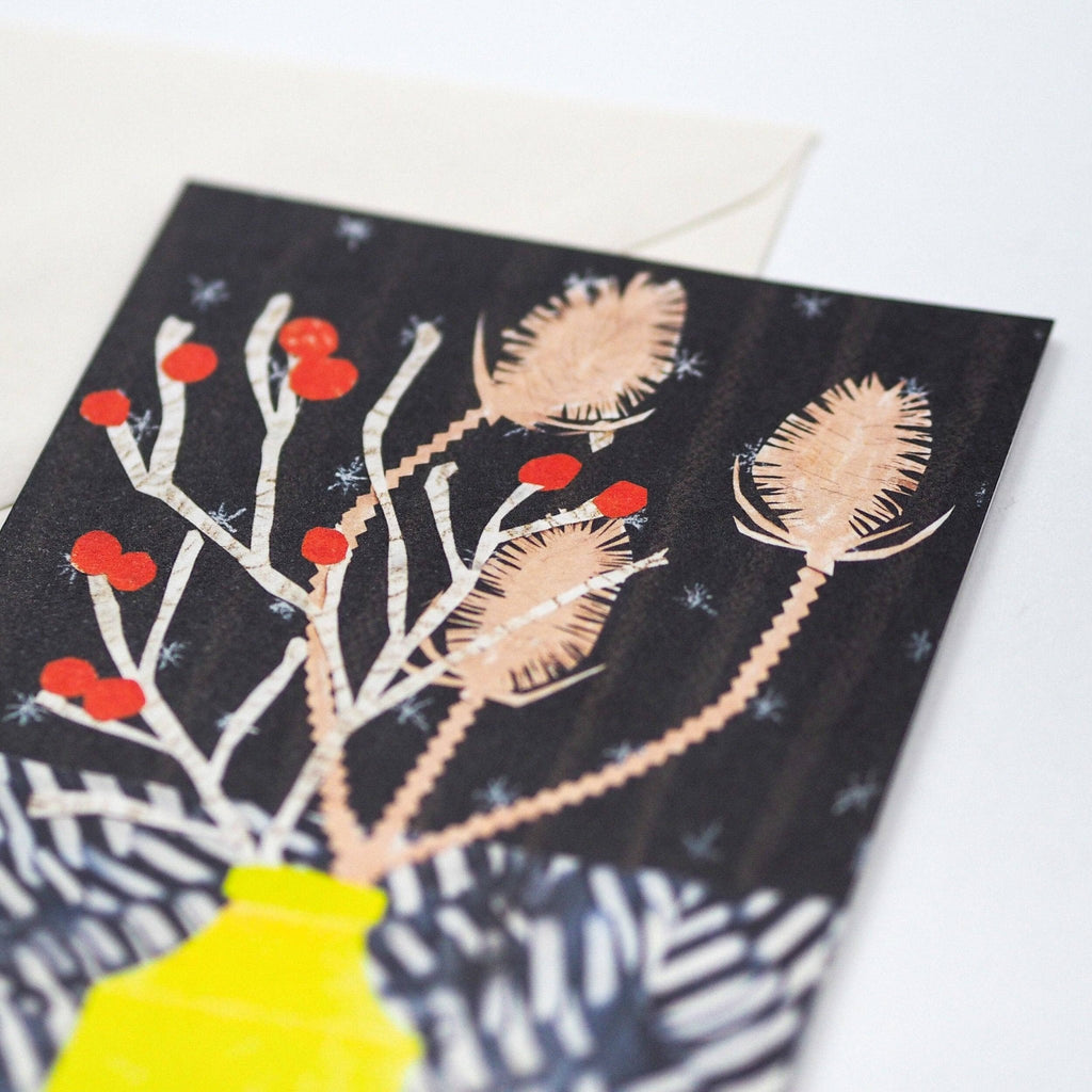 Close up of a greetings card featuring a stylised bouquet of winter berries and teasels in a yellow vase - All Good Things